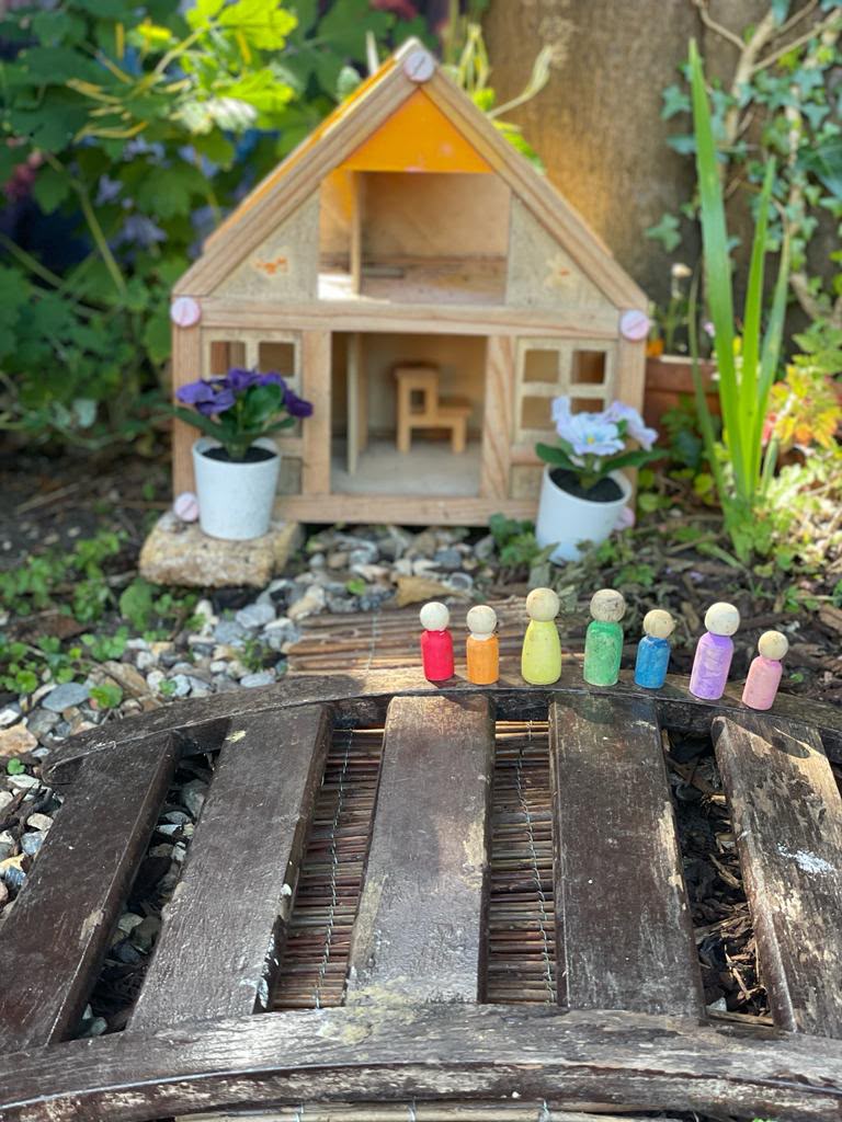 Peg dolls lined up outside a wooden fairy house