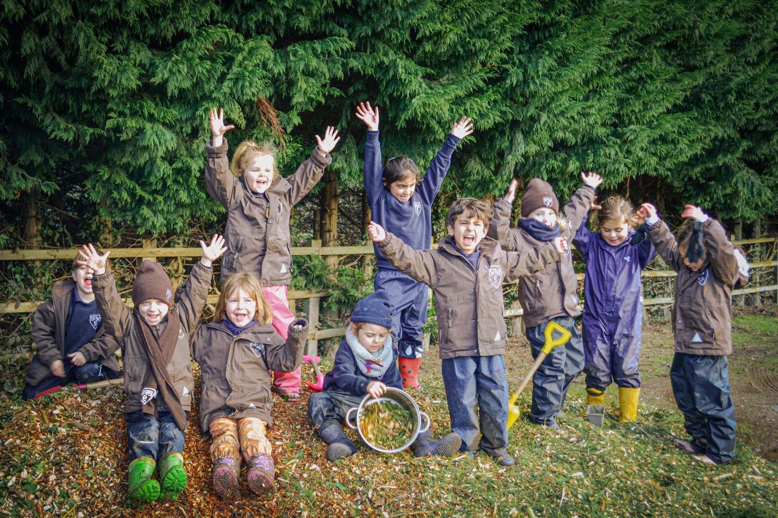 A group of children in muddy waterproofs cheering with hands in the air