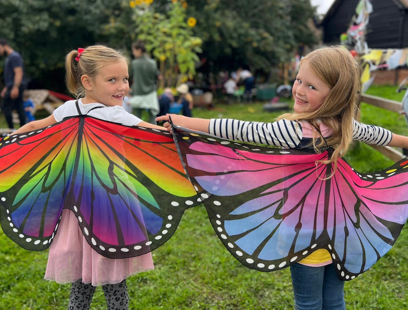 Two girls wearing rainbow butterfly wings in the WildOnes garden