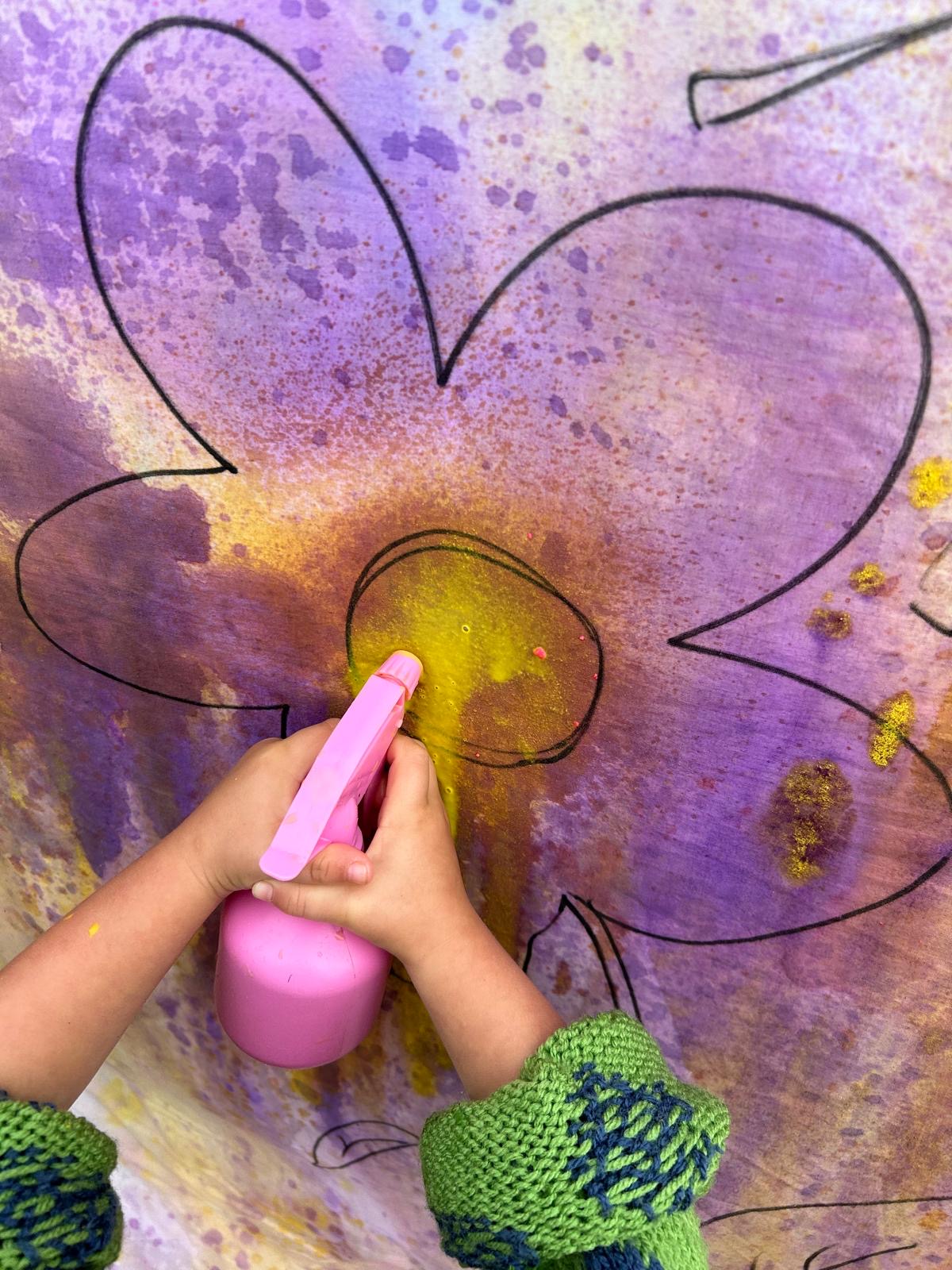 A child spraying colour onto a big painted flower