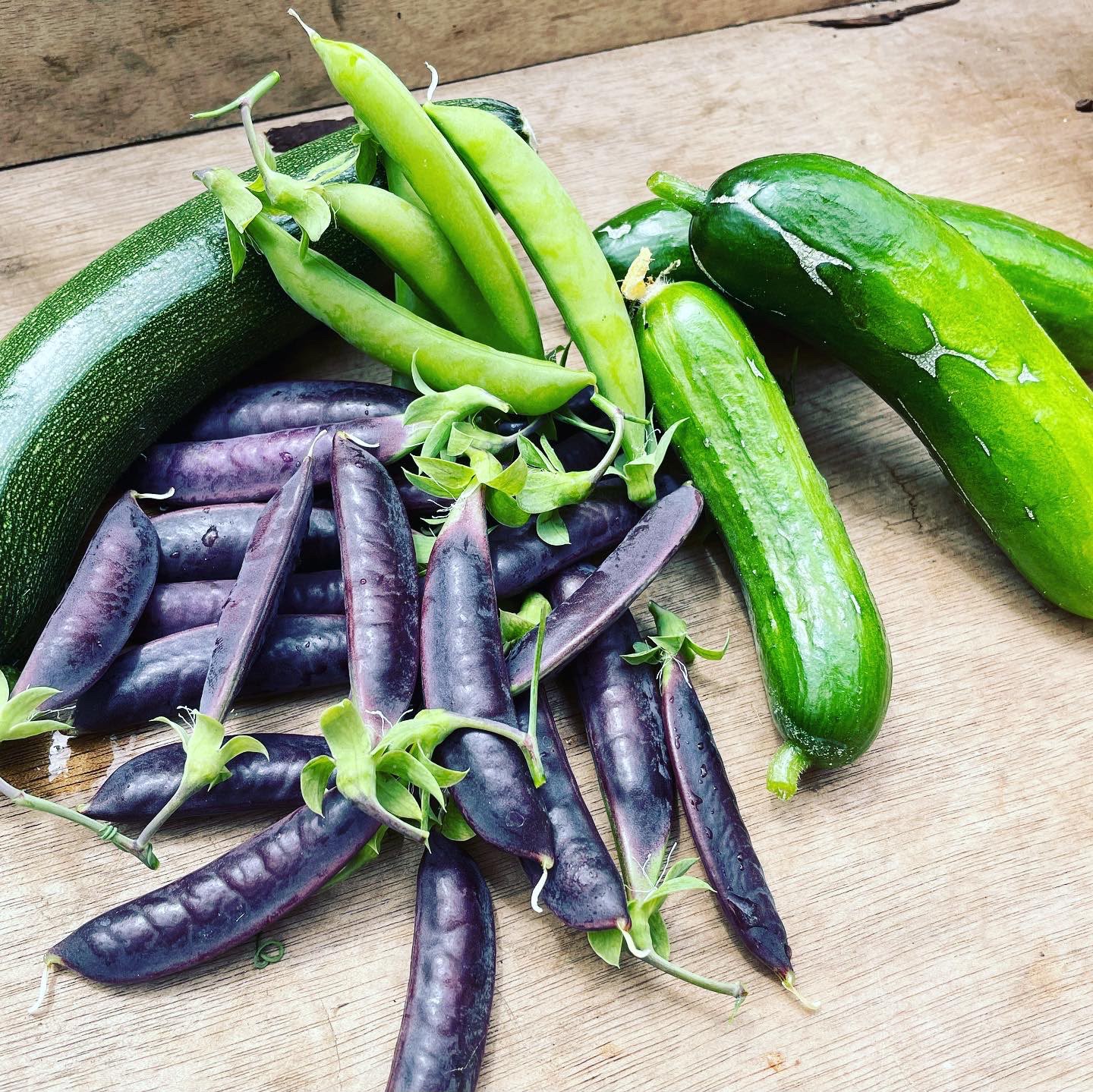 Courgettes, cucumbers and purple peas on a wooden board