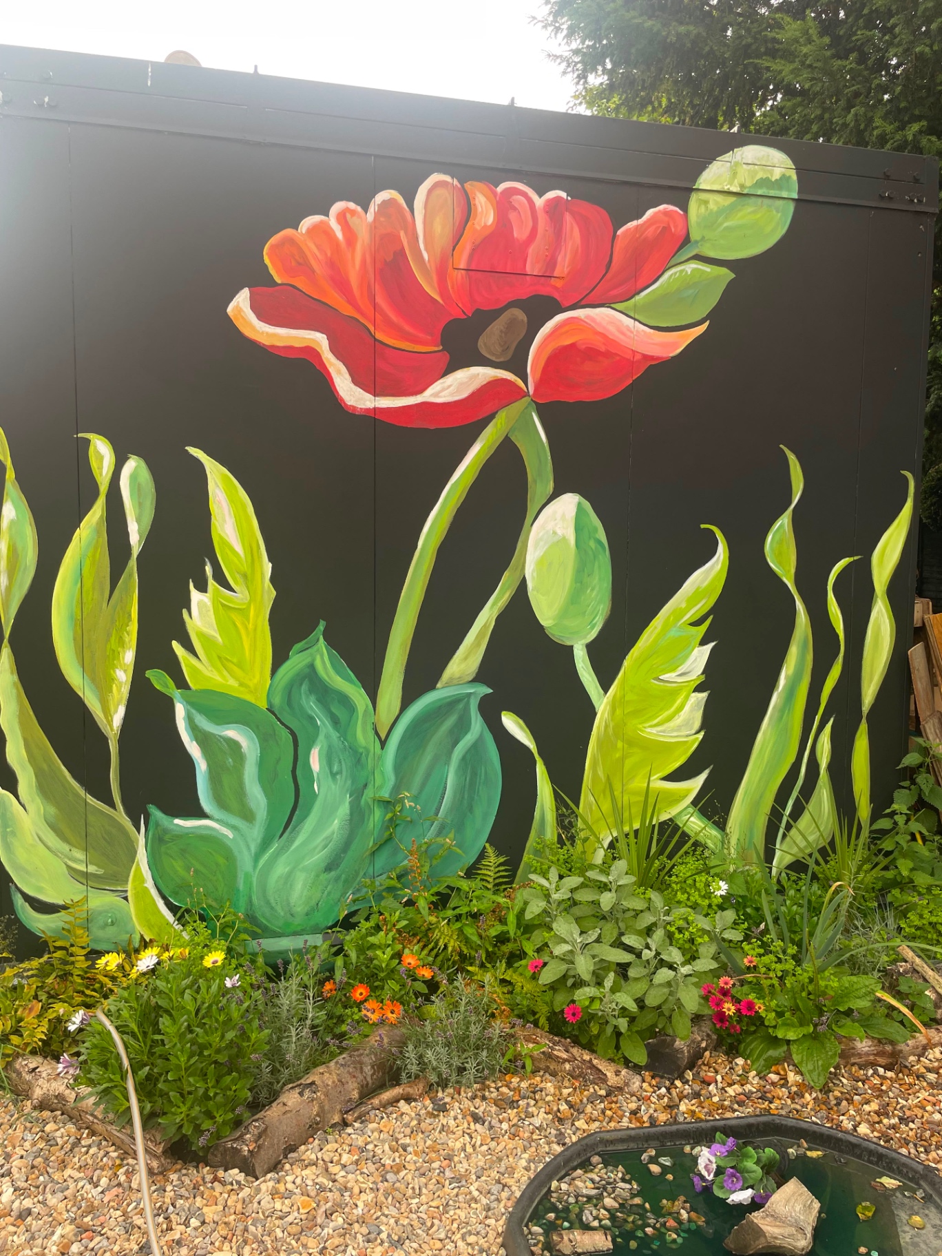 A hand-painted poppy mural above a flower bed